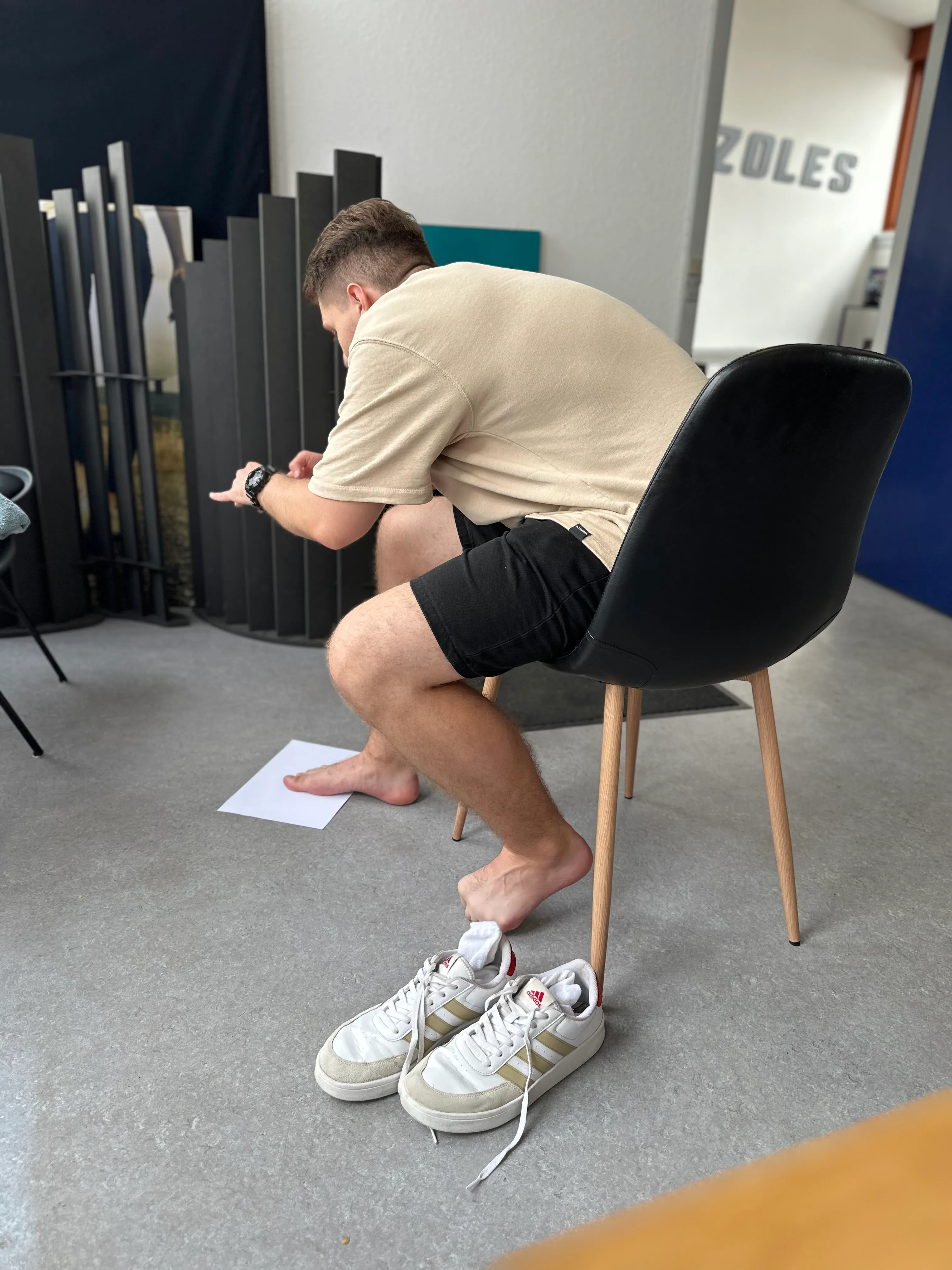 Person seated in ZOLES clinic testing mobile app foot scanning functionality, demonstrating the app development and testing process in professional environment